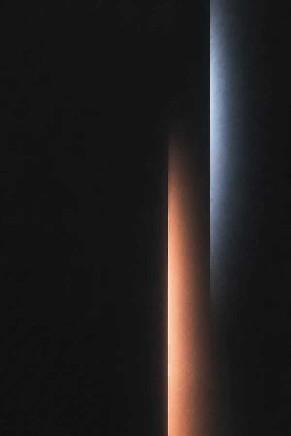 A dark charcoal portrait abstract with two tall vertical light bands on the right: a peach glow rising from the bottom and a silver-blue band extending from…
