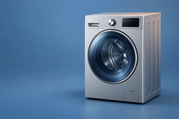 A silver front-loading washing machine stands right of centre against a seamless blue background and floor, shown from a front three-quarter angle with open…
