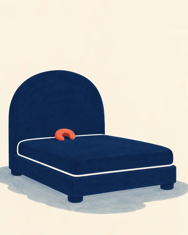A broad midnight-blue bed with a tall rounded arch headboard, thick mattress and short feet sits on a muted blue-gray shadow against a warm ivory background.