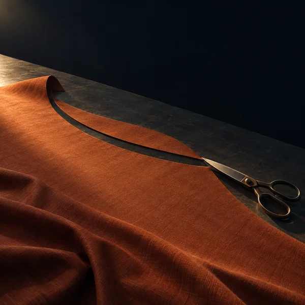 A rust-colored woven fabric sheet lies across a dark cutting table, with a sweeping curved cut and a pair of steel shears at its endpoint.