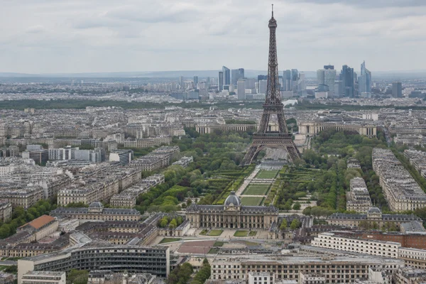 A high view over Paris shows the Eiffel Tower above the green Champ de Mars, with a large pale-stone complex and central dome in the foreground and a cluster…
