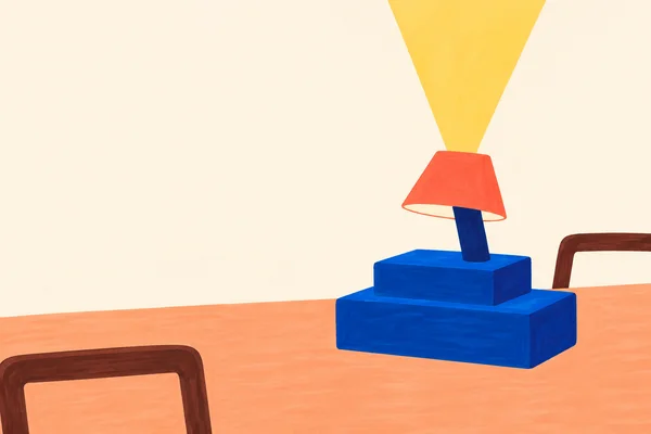 A squat blue two-tier desk lamp with a short stem and coral trapezoid shade sits on a peach tabletop.