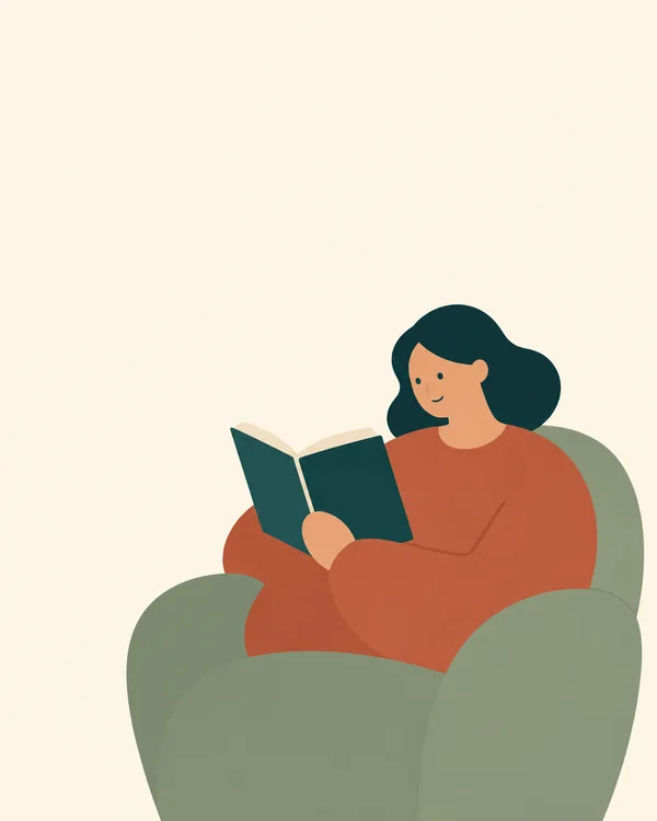 A person with dark teal hair reads an open dark teal book while seated in a large sage-green armchair against a warm cream background.