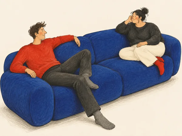 Two adults lounge at opposite ends of a large blue sofa, facing each other.