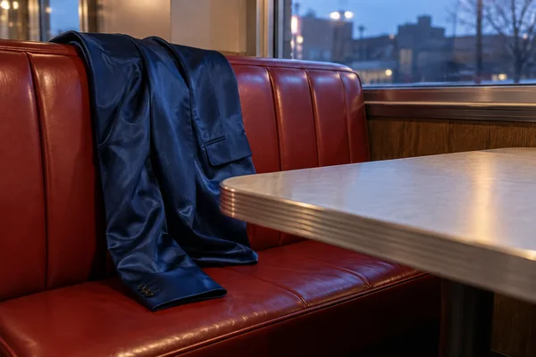 A dark blue satin jacket hangs loosely over a cherry-red restaurant booth, with one sleeve resting on the seat.