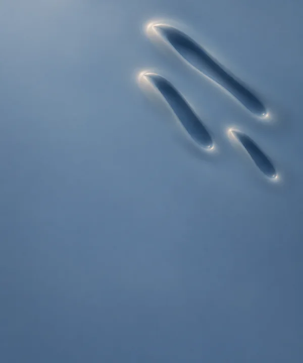Three elongated dark-blue depressions with soft ivory rims sit on a slate-blue liquid-like surface, clustered diagonally in the upper-right area above broad…
