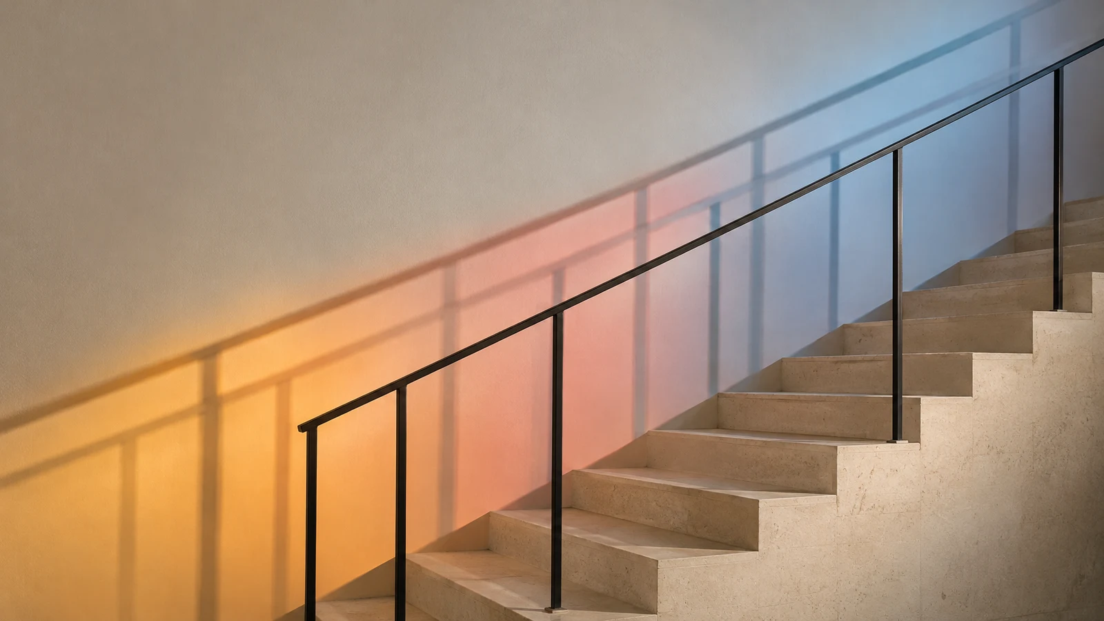 A pale stone staircase with a slender dark metal railing rises across the frame, while overlapping amber, coral and blue light cast several railing shadows…