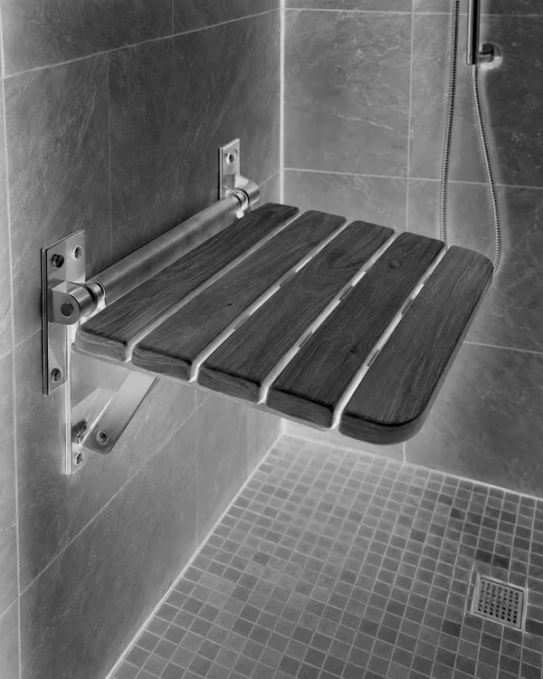 A horizontally lowered wooden slatted shower seat projects from tiled walls above a small-tile shower floor, with metal wall brackets, a shower hose and a…