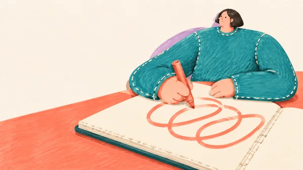 A person in a turquoise sweater sits behind an oversized open cream sketchbook on a coral desk, holding a coral marker and drawing broad loops across the page.