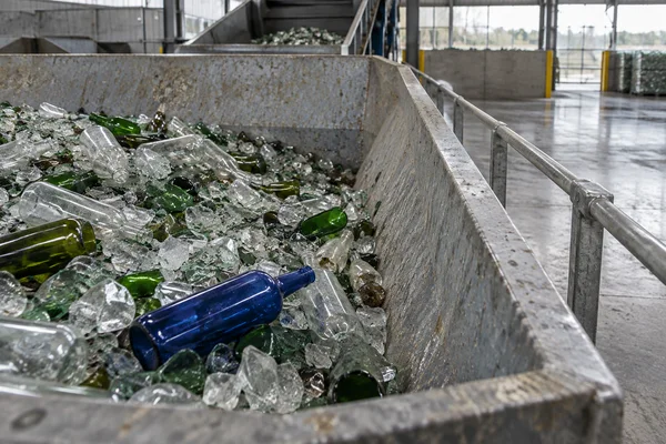 A cobalt-blue bottle lies diagonally among clear and green glass bottles and fragments in a large galvanized-steel hopper.