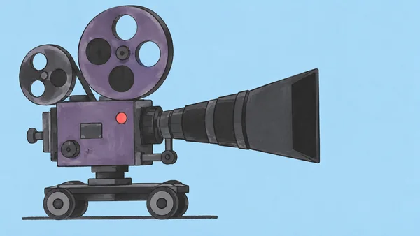 A large vintage-style movie camera with two unequal reels and an elongated charcoal lens sits on a two-wheeled dolly against a pale blue background.