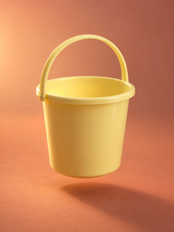 A pale yellow plastic bucket with an upright arched handle floats above a terracotta-colored floor, shown from slightly above so its empty interior is visible.
